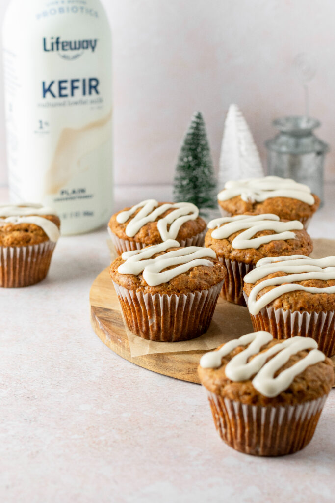 Gingerbread muffins sitting on a platter with mini christmas trees and a bottle of milk in the background.
