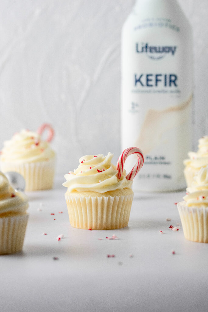 White chocolate cupcakes with peppermint candies and milk in the background.