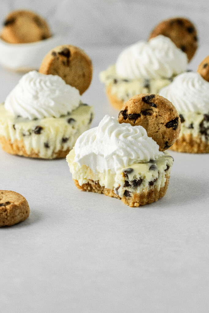 Mini cheesecakes with a bite taken out of it and mini chocolate chip cookies on the side.