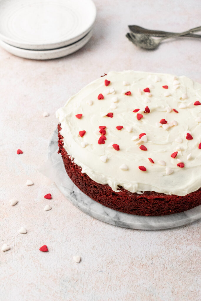 Mini red velvet cake recipe topped with cream cheese frosting and heart sprinkles.