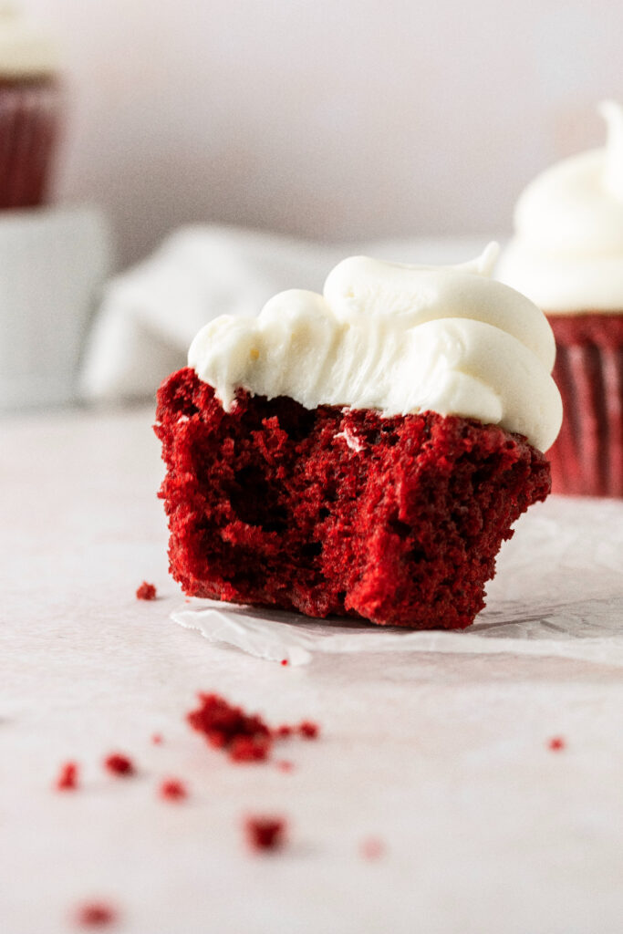 A frosted red velvet cupcake with a bite taken out of it.