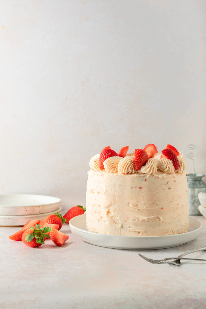 Frosted banana strawberry cake with fresh strawberries. White plates and forks are in the background.