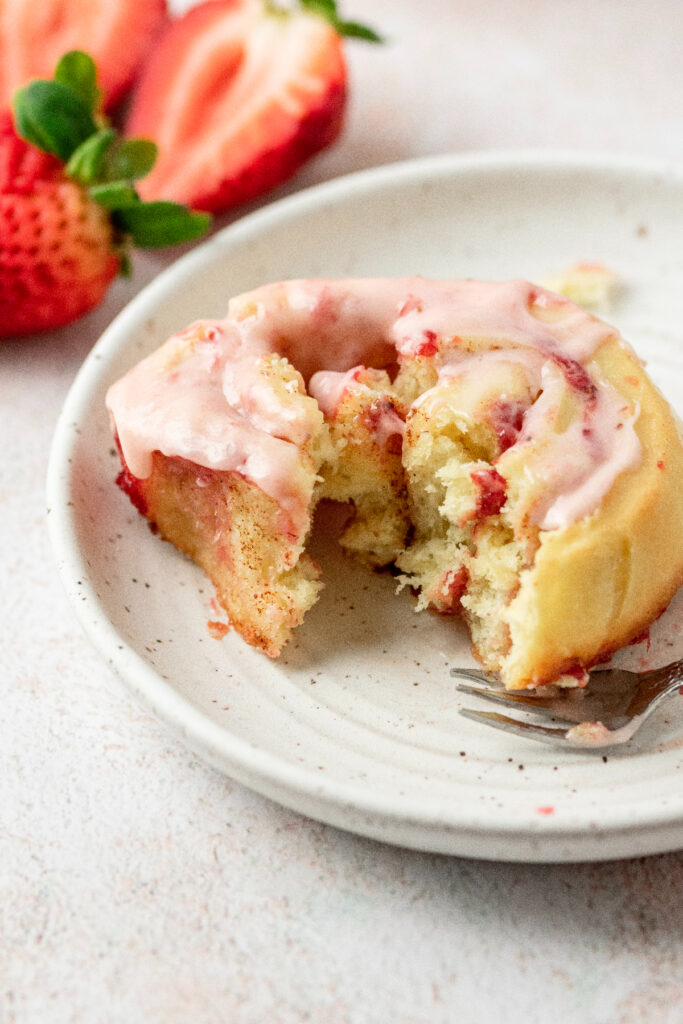 Strawberry cinnamon roll on a white plate with a bite taken out of it.