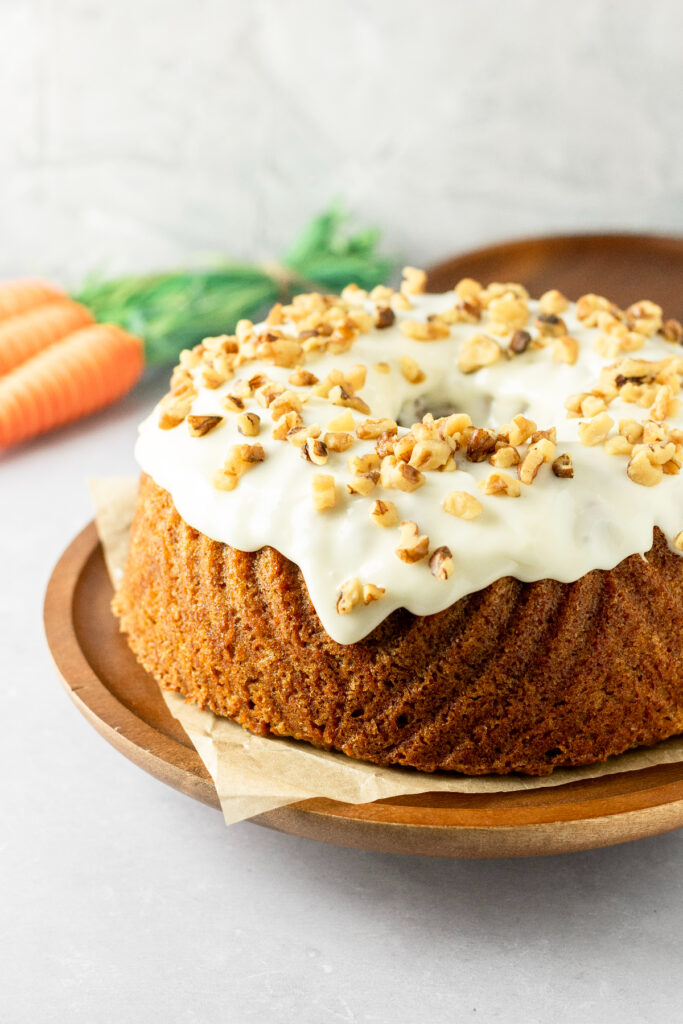 Cream cheese frosted carrot cake with carrots in the background.