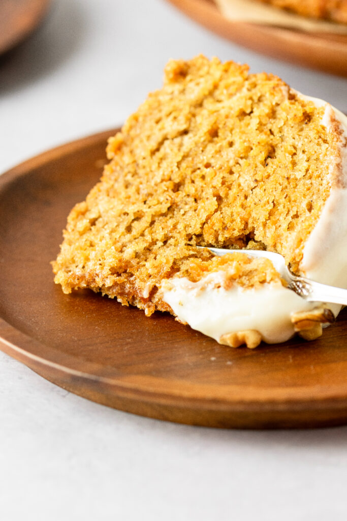 Carrot pound cake slice on a brown plate with a fork slicing through it.