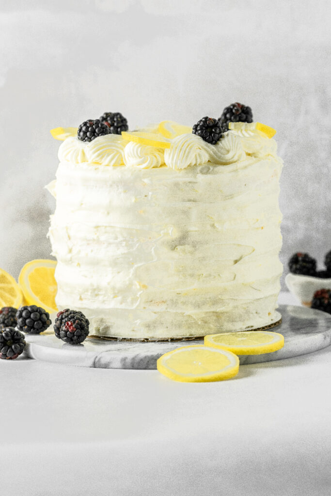 Frosted lemon cake on a marble cake stand.