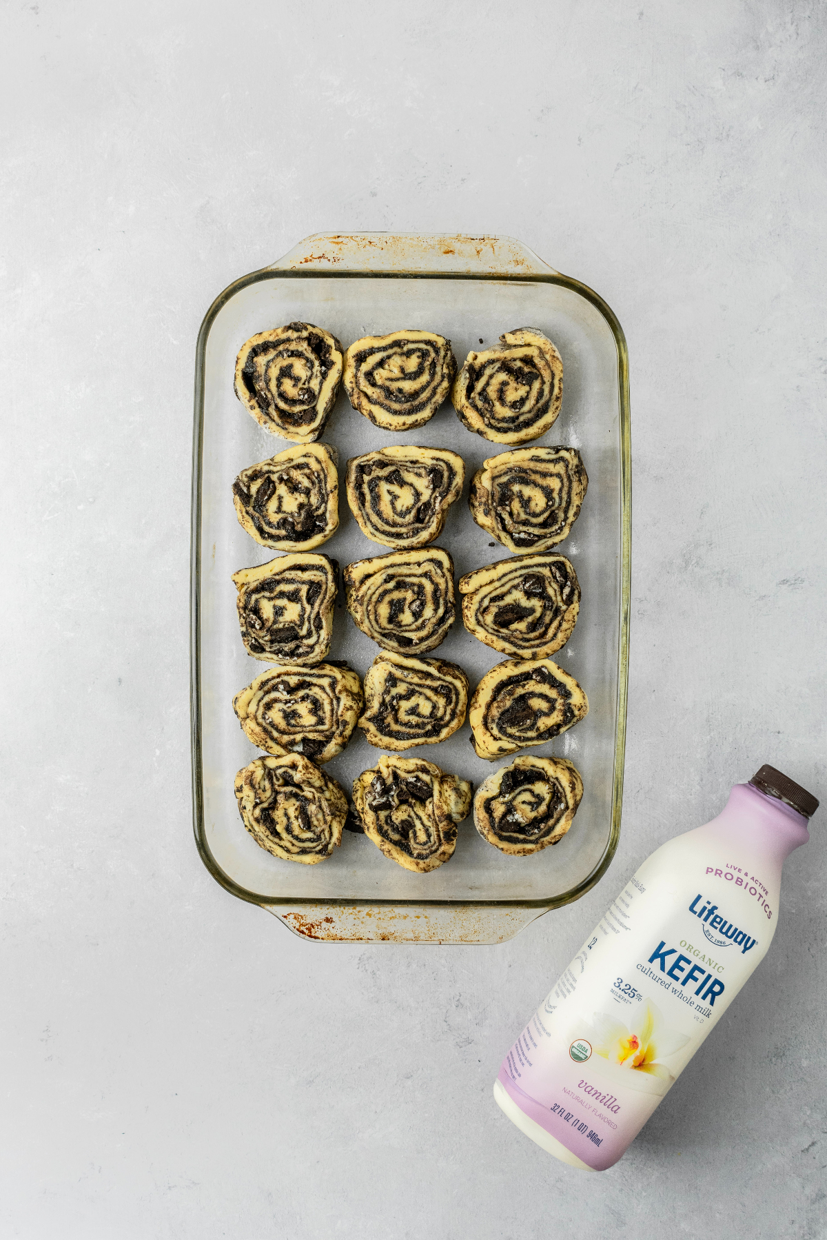 Cinnamon roll slices in a glass baking pan with a bottle of Kefir.