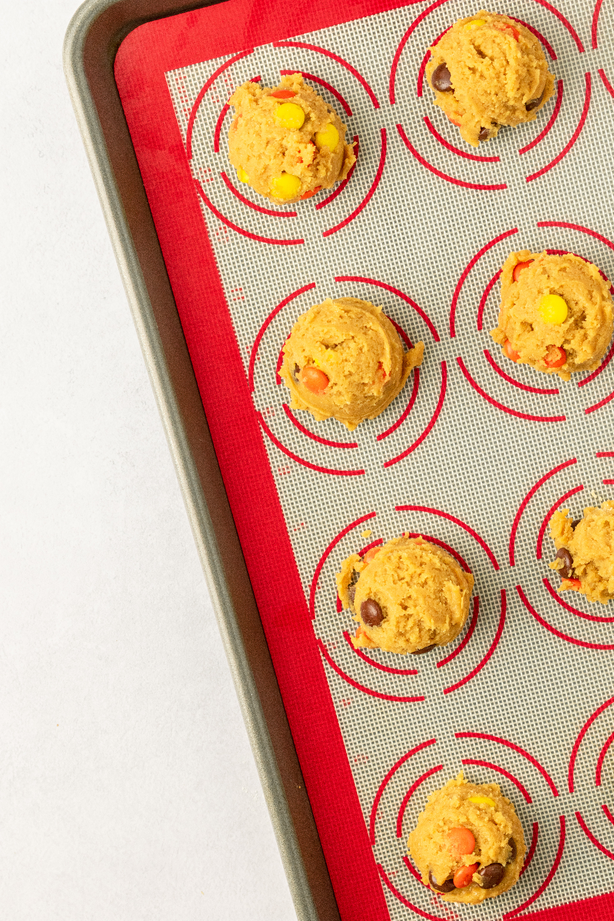Cookie dough balls on a baking sheet with candy on top.