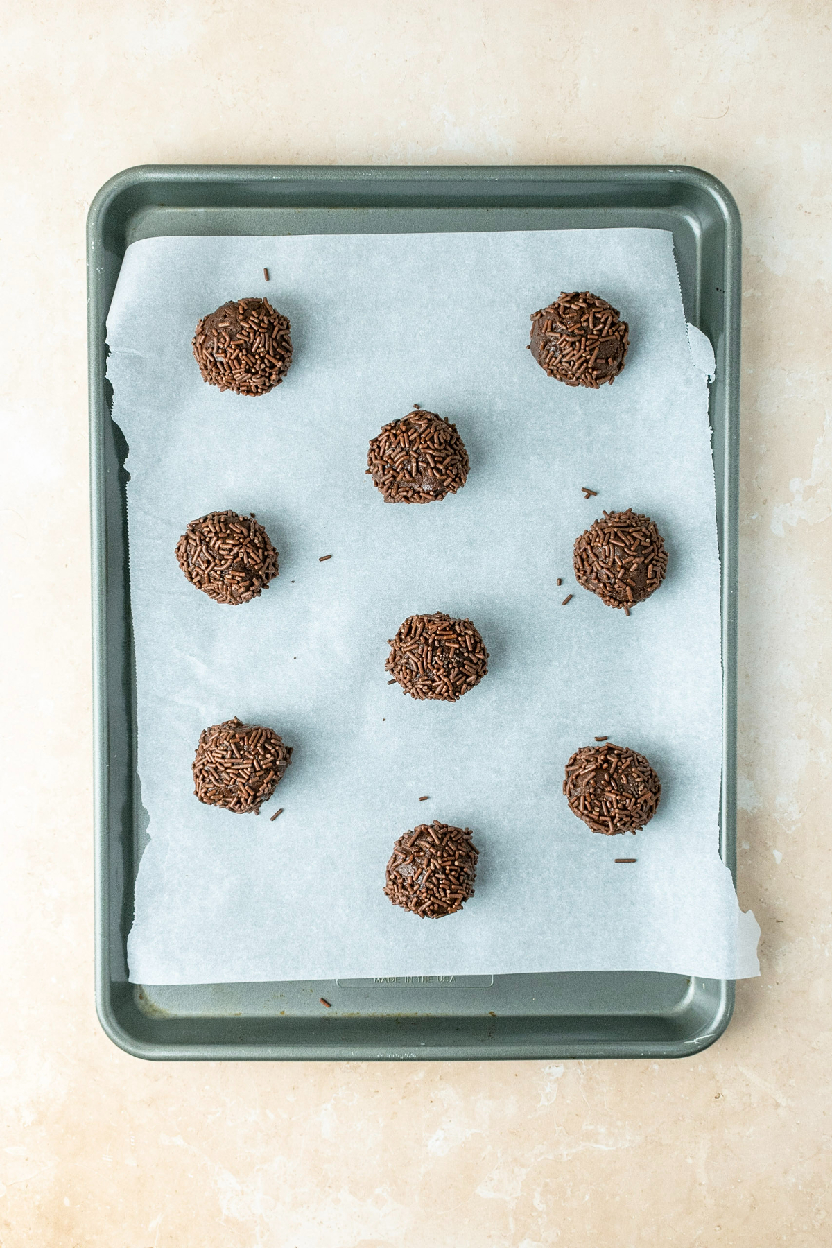 Chocolate cookie dough balls on a parchment paper lined baking sheet.