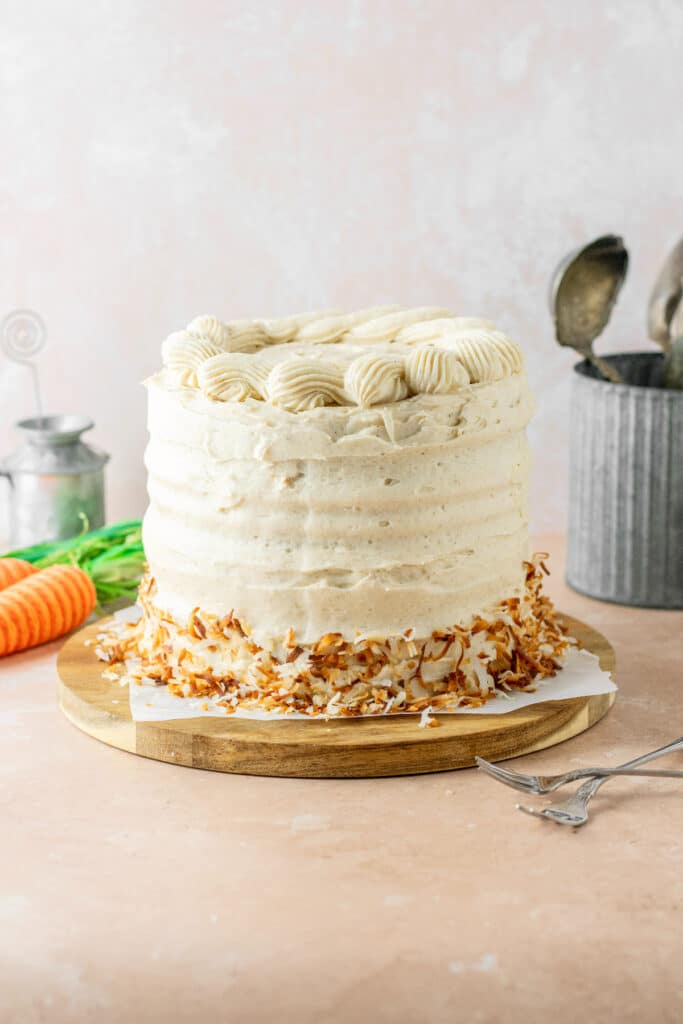 Cream cheese frosted with toasted coconut carrot cake with forks and carrots on the side.