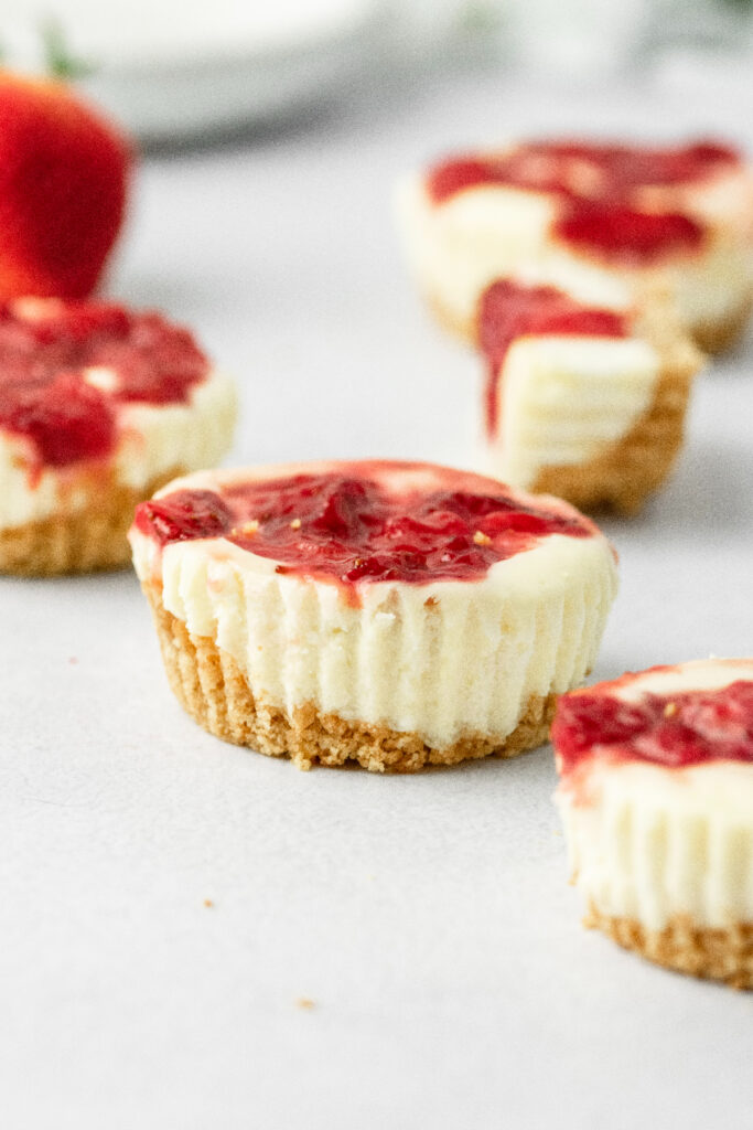 Mini cheesecakes with graham cracker crust and strawberry sauce.