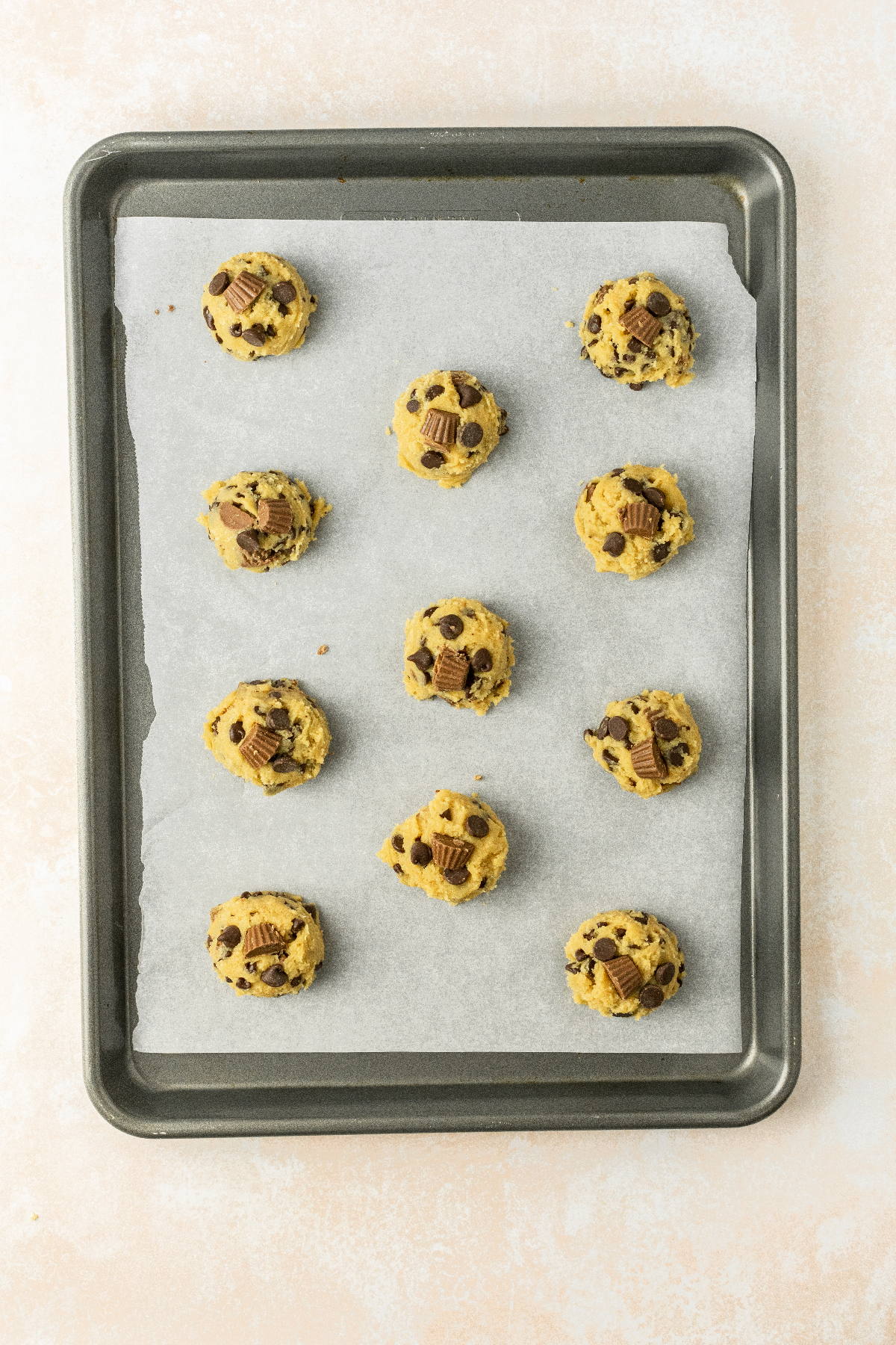11 cookie dough balls on a parchment lined baking sheet.