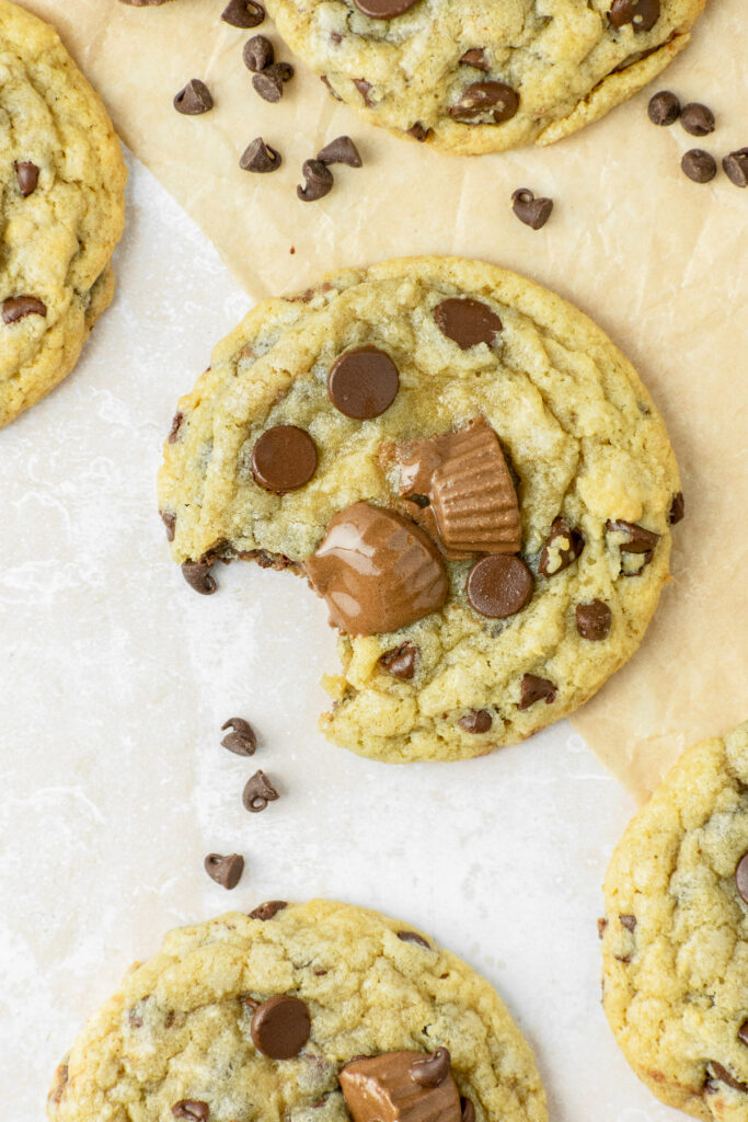 A cookie with a bite taken out of it and chocolate chips all around the parchment paper.