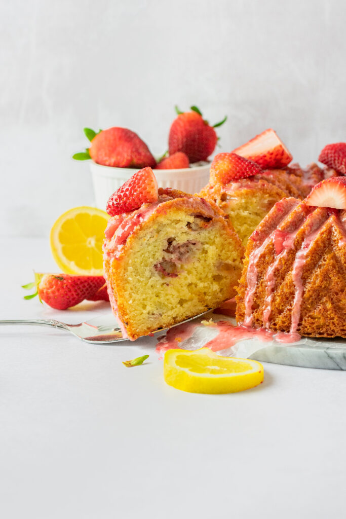 Strawberry cake slice on a marble cake board with fresh strawberries and lemon slices.