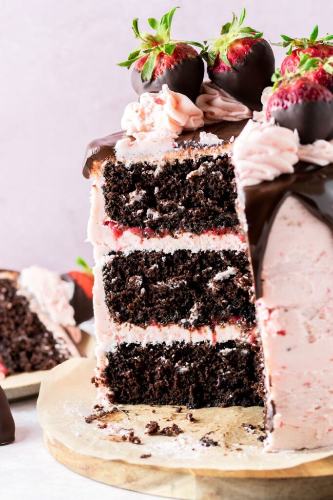 Looking inside at a chocolate covered strawberry cake topped with chocolate strawberries, chocolate ganache, and strawberry frosting.