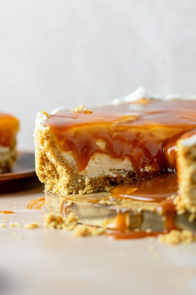 Vanilla cheesecake with a graham cracker crust and caramel sauce dripping off of the sides.
