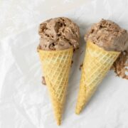 Two ice cream cones with chocolate ice cream and a wooden spoon on the side.