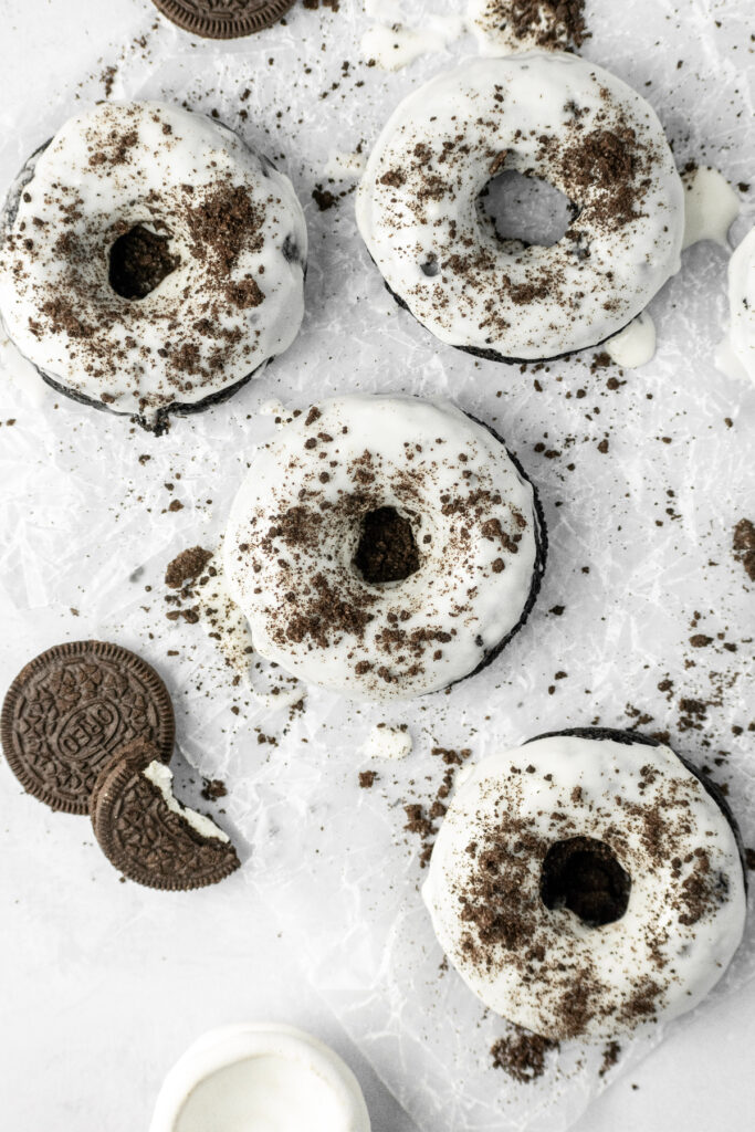 Five vanilla glazed donuts with Oreo cookies and crumbs on the side.