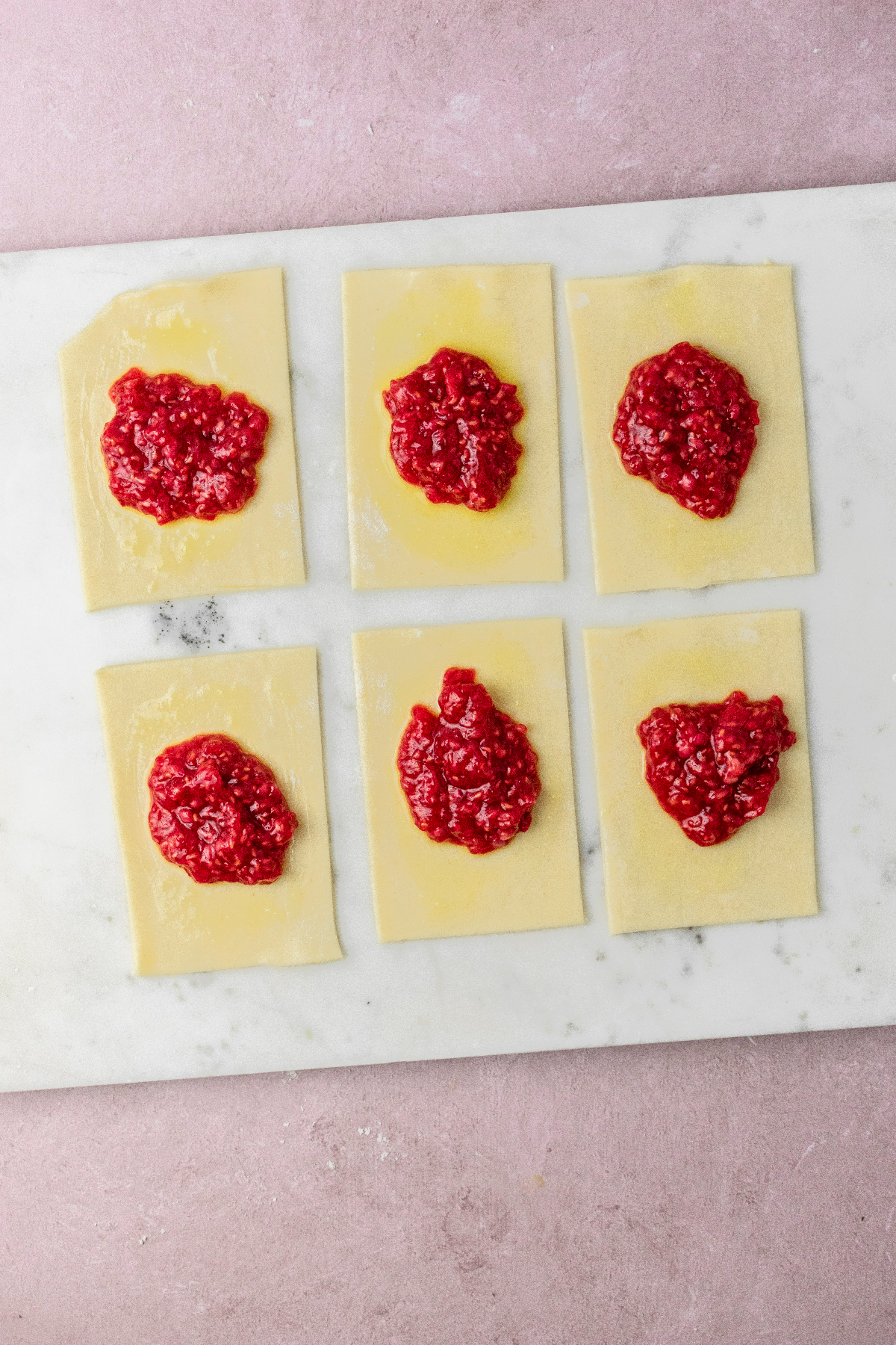 Pie dough cut into rectangles and being filled with raspberry jam.