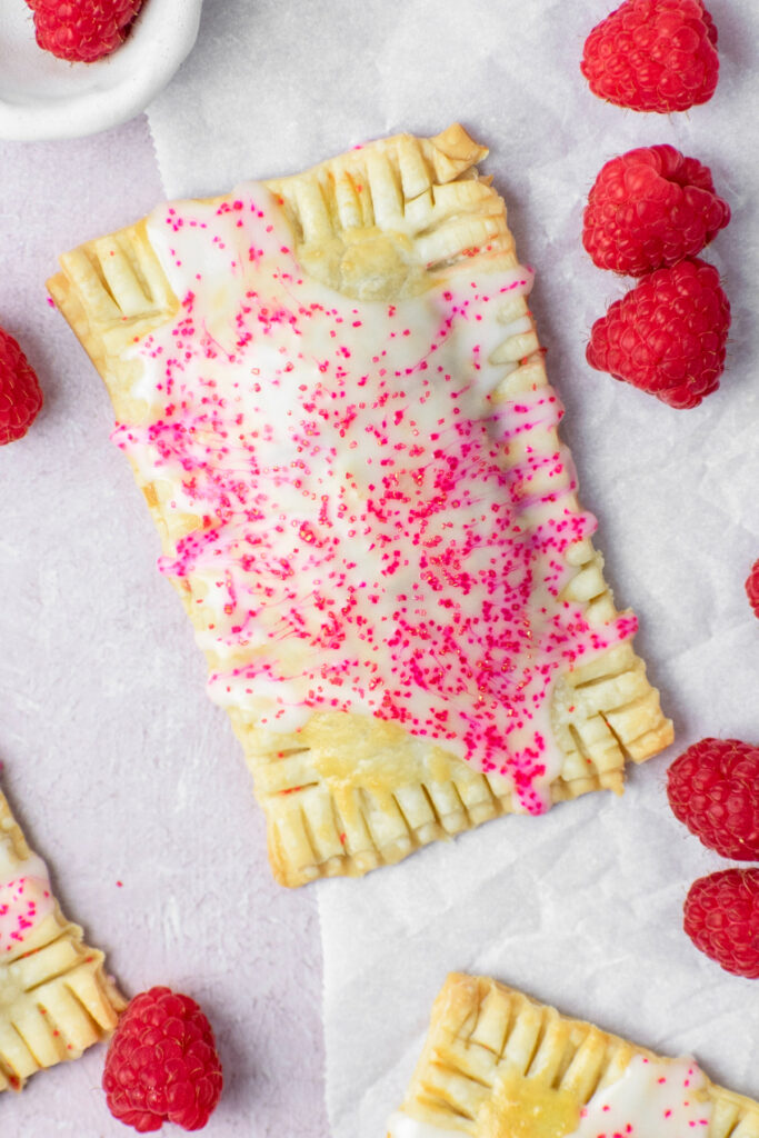 Pop tarts sitting on parchment paper with raspberries.