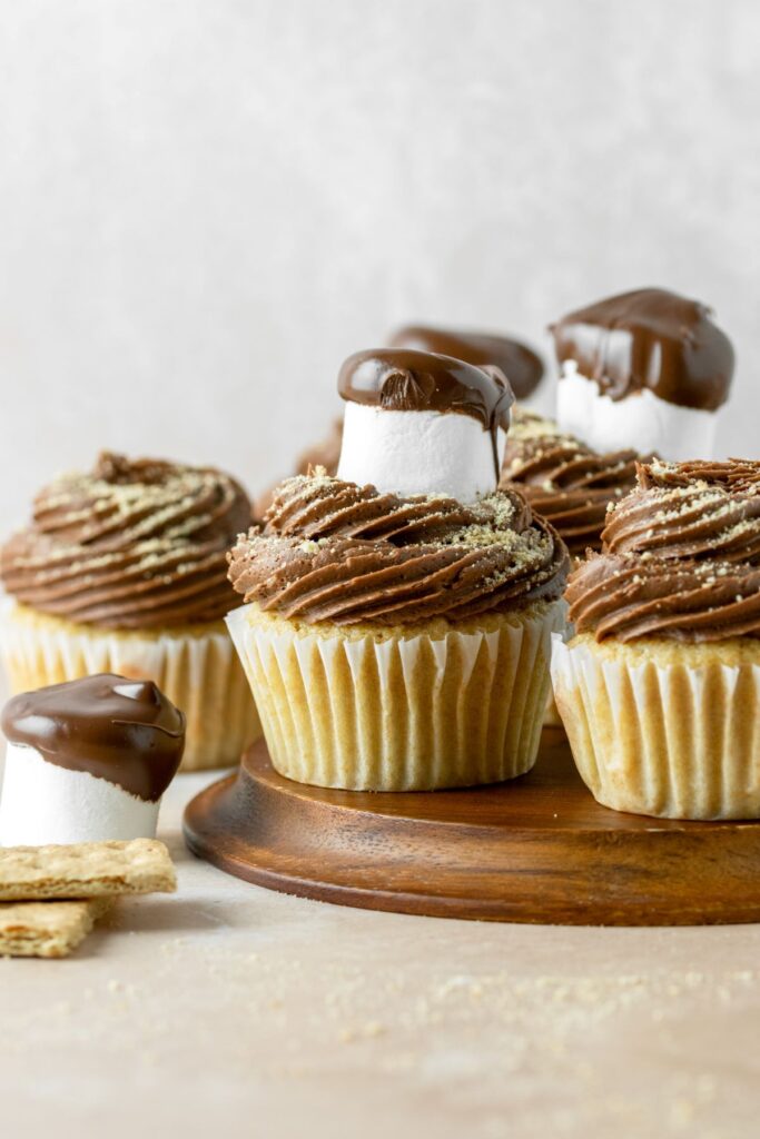 S'mores cupcakes on a brown plate with a chocolate dipped marshmallow and graham crackers.