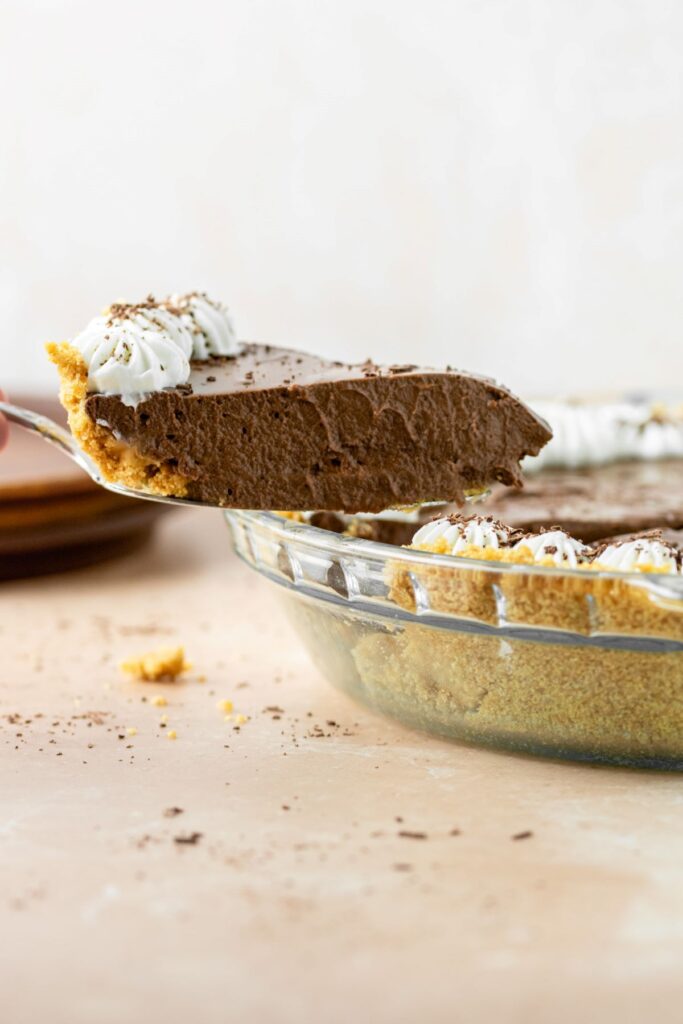 A piece of chocolate pie with graham cracker crust being removed from the pie plate.