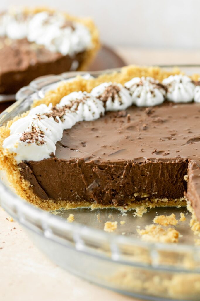Chocolate pudding pie sitting on a graham cracker crust with dallops of whipped cream on top.