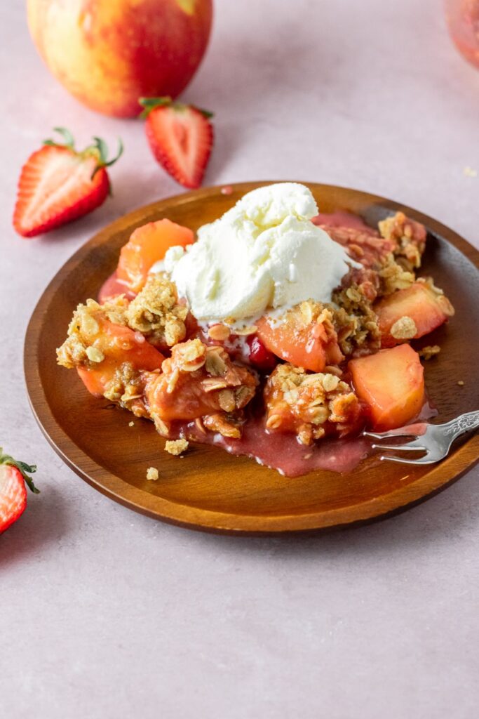 Fruit crumble with strawberries and apples on a plate with a fork and strawberry halves.