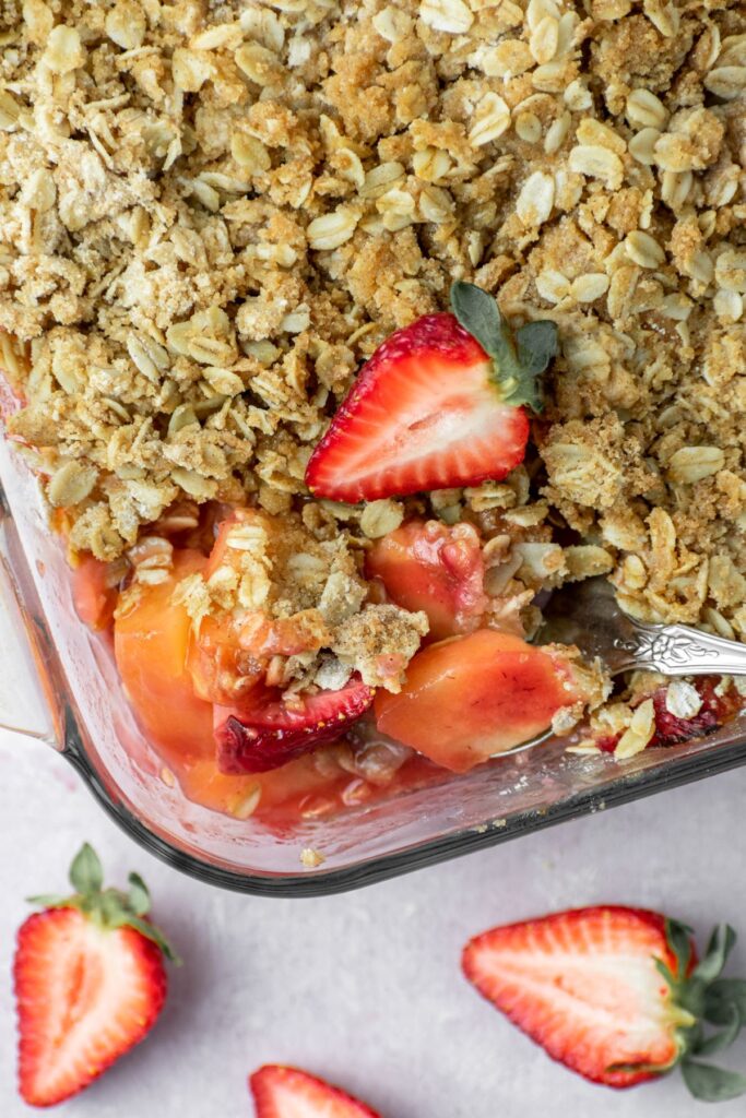 Fruit crisp in a baking pan with fresh strawberries on top and a streusel crumble.