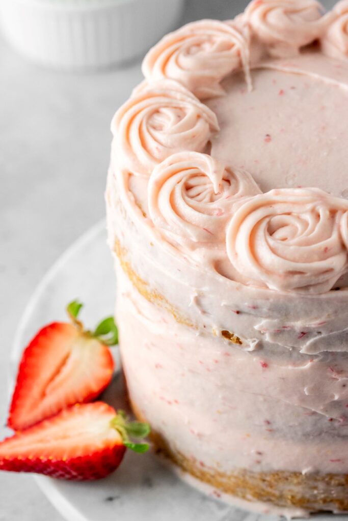 Strawberry naked cake on a cake plate with sliced strawberries.