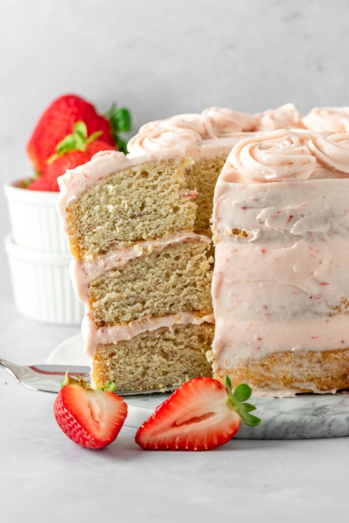 A slice of strawberry cake with with strawberries on the side on a cake plate.