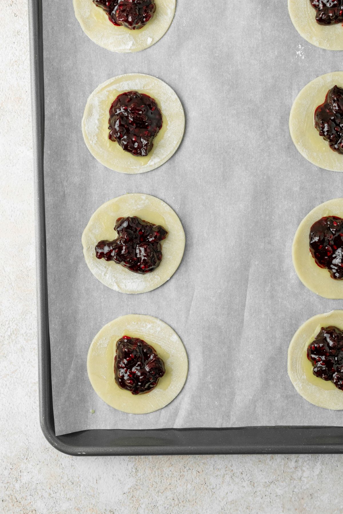Pie circles filled with blackberry jam on a parchment paper lined baking sheet.