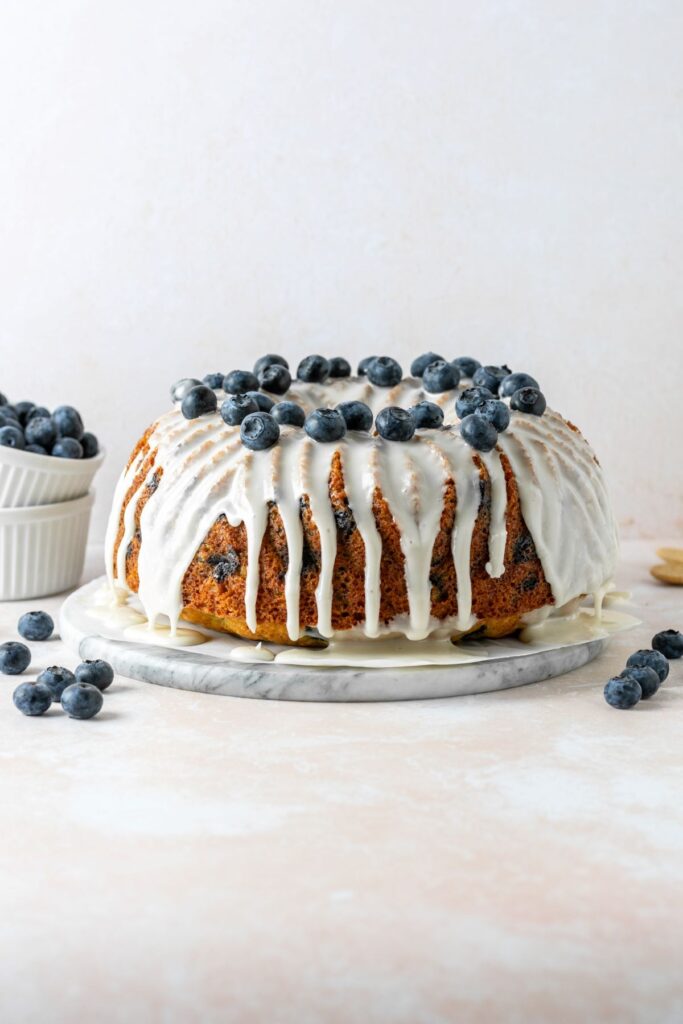 A bundt cake that is topped with vanilla icing and a lot of fresh blueberries.