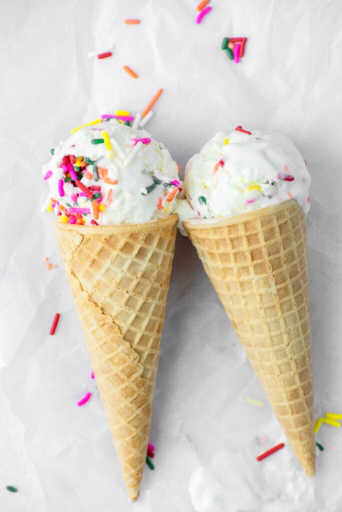 Two waffle cones with vanilla ice cream and colorful sprinkles.