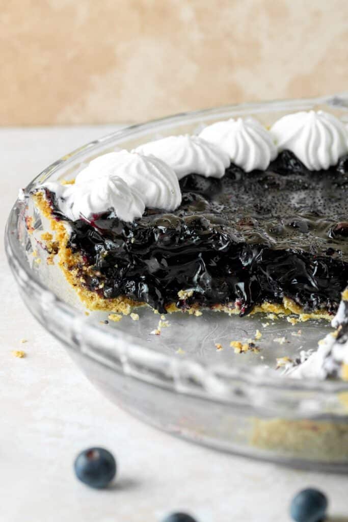 Blueberry pie with a graham cracker crust and whipped cream dollops.