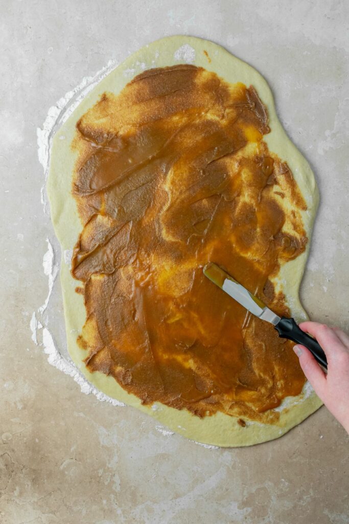 Caramel being spread over the cinnamon filling on top of the rolled out dough.