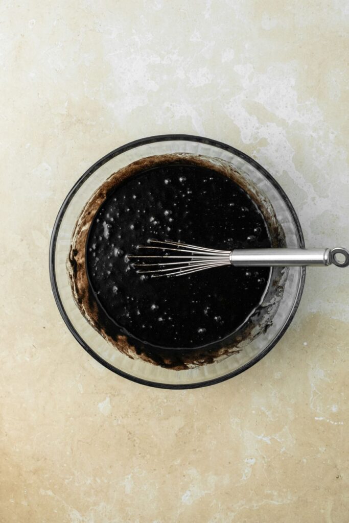 Black cocoa powder cupcake batter in a glass bowl with a metal whisk.