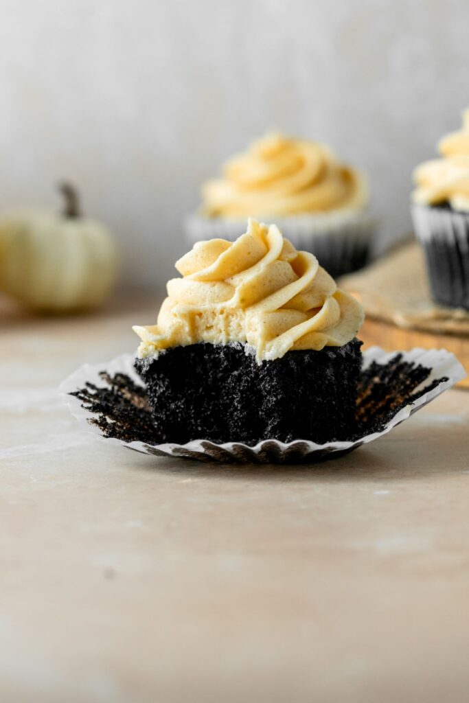 A pumpkin chocolate cupcake sitting on a cupcake liner with a bite taken out of it.