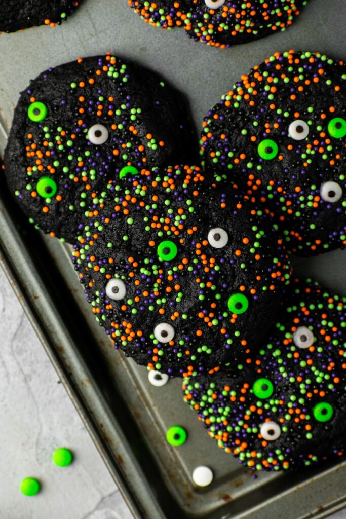 Black velvet cookies on a baking sheet with green and white eyeballs on top.