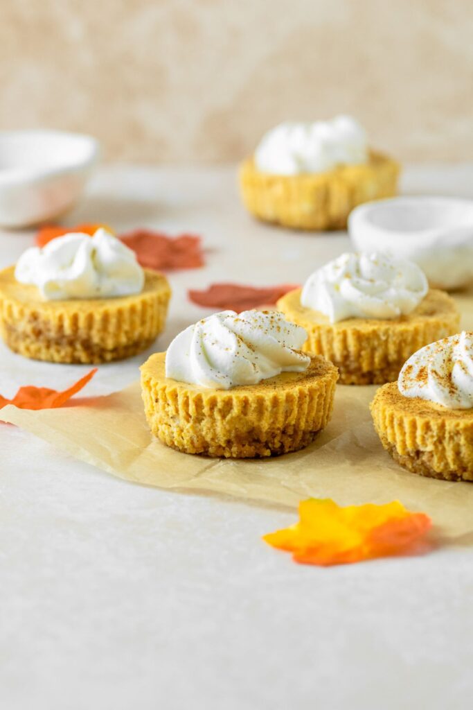 Mini cheesecakes with a gingersnap cookie crust surrounded by colorful leaves.
