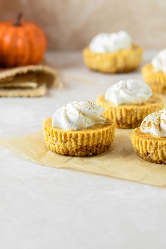 Mini pumpkin cheesecakes sitting on brown parchment paper.