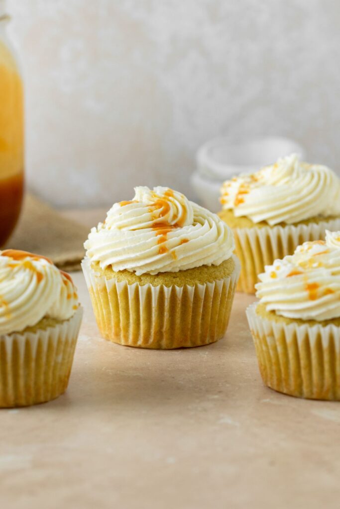 Frosted cupcakes with a jar of caramel in the background.