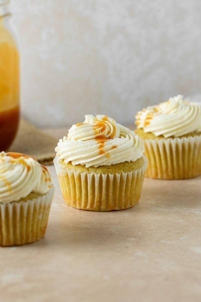 Caramel cupcakes with buttercream frosting and caramel drizzle on top.