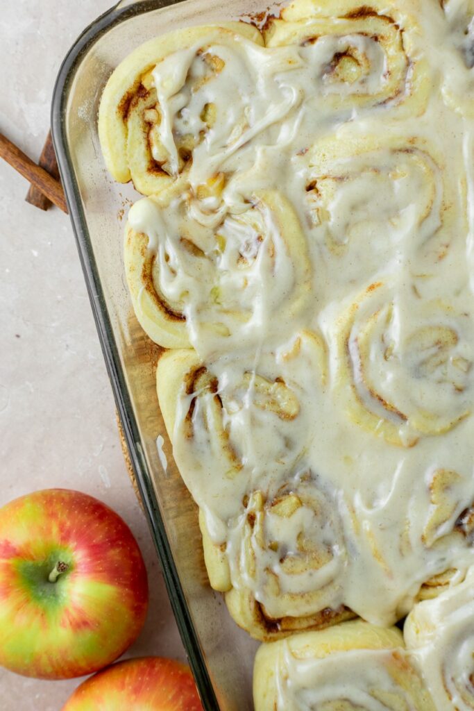 Cinnamon rolls with apple pie filling in a glass baking pan covered with cream cheese icing.