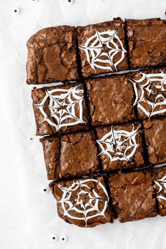 Dark chocolate brownies cut into squares with white web designs on top.