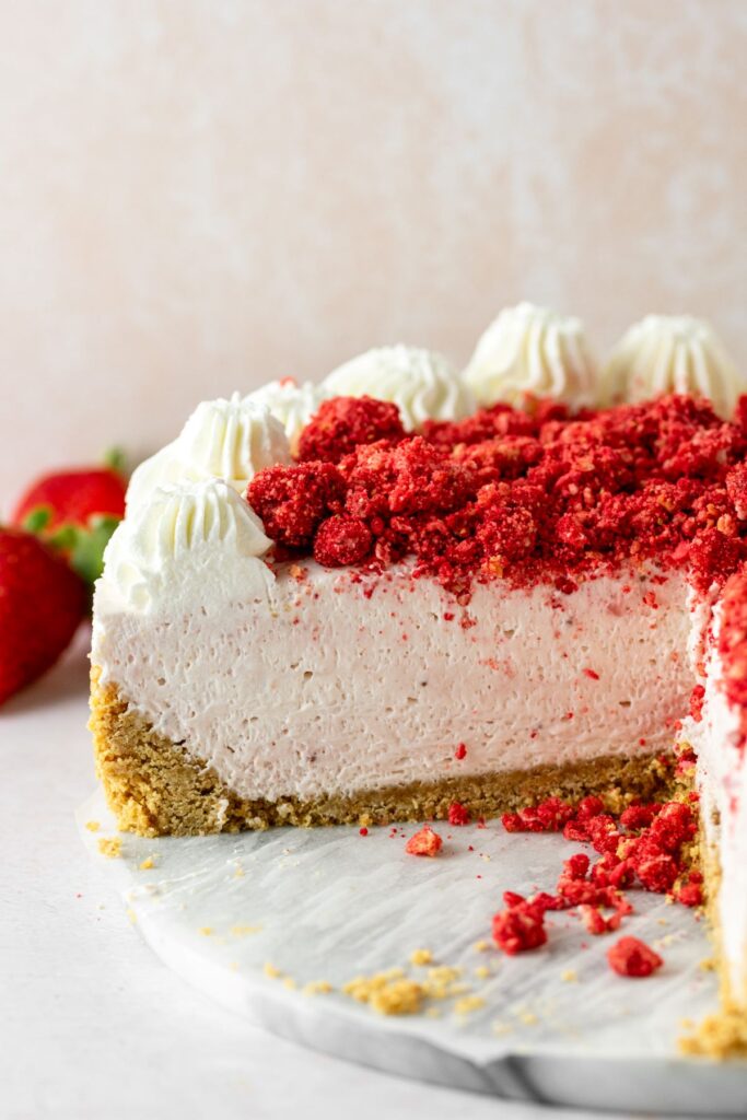 Strawberry crunch cheesecake with graham cracker crust. It has a crunchy strawberry topping and dollops of whipped cream.