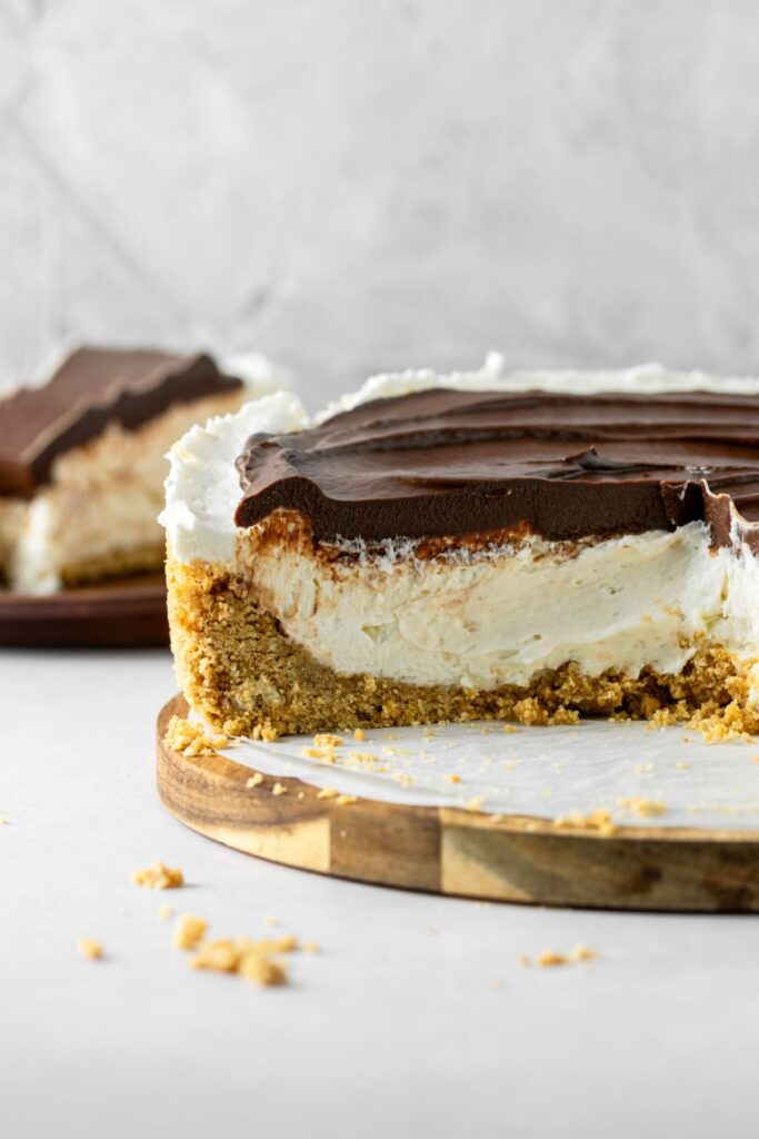 Vanilla cheesecake with chocolate ganache topping. It has a graham cracker crust and is sitting on a wooden cake plate.
