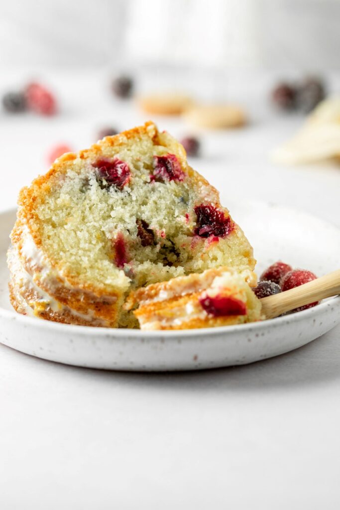 A slice of cranberry pound cake on a white plate with fresh cranberries bursting through.
