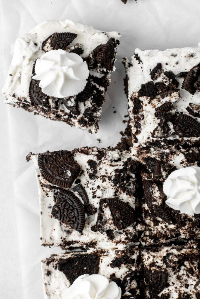 Cookies and cream cheesecake squares with dollops of whipped cream on top.