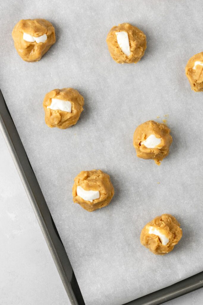Peanut butter cookie dough balls with marshmallows in the center on a baking sheet.